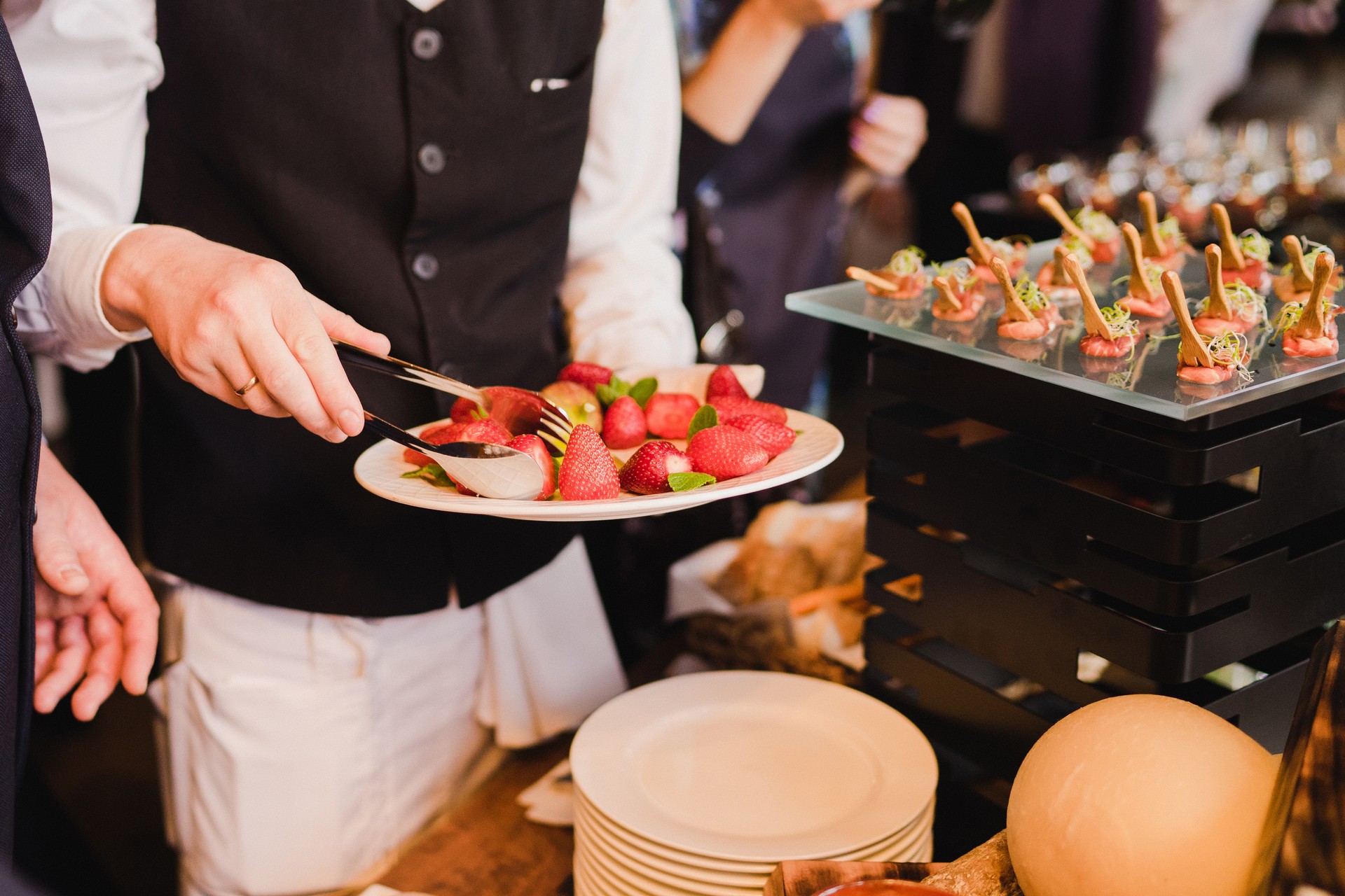 Waiter serving strawberry near catering banquet table at wedding reception.